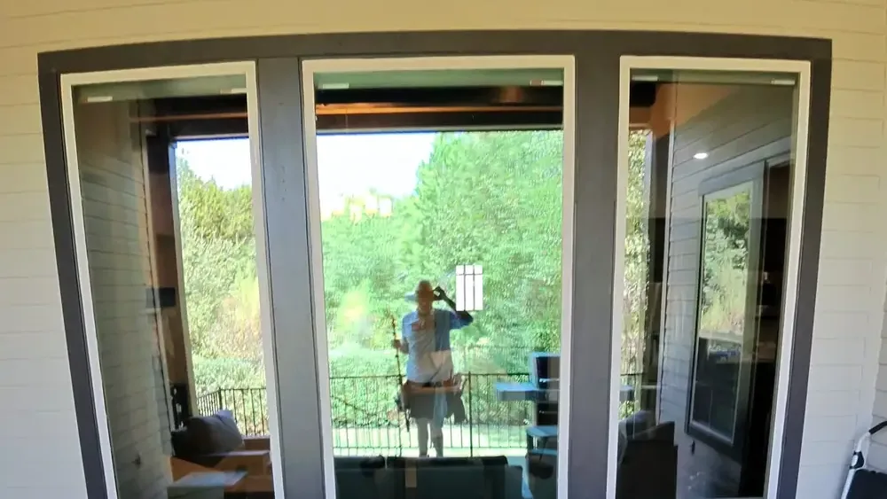 A three panel window on a covered patio, cleaned, with Mason reflected in the middle pane holding his water fed pole