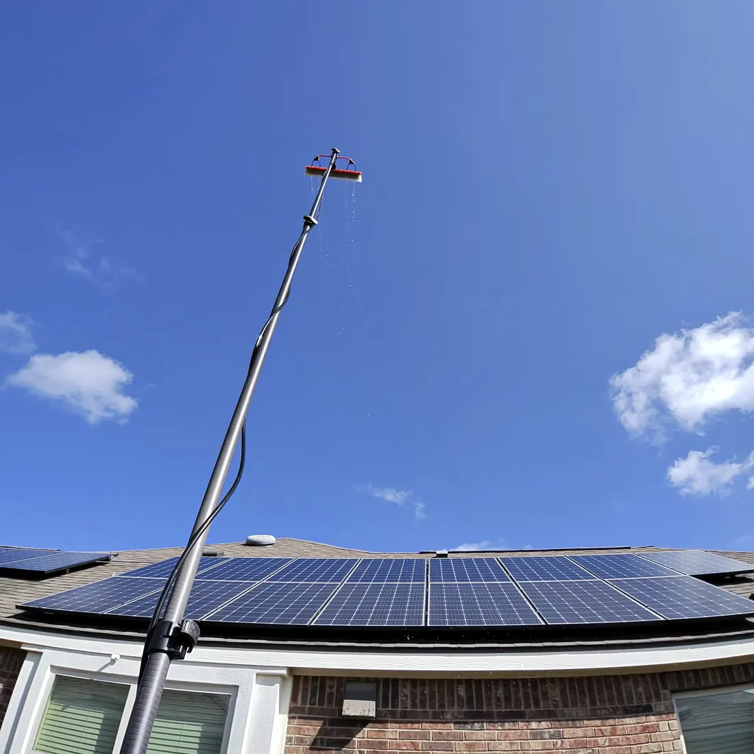 Water-fed pole extended above a roofline to clean a rooftop solar array