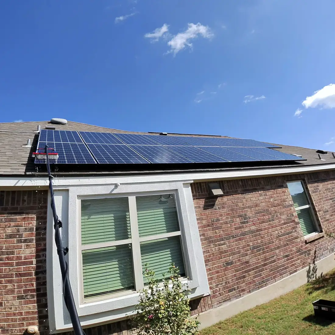Brush head rinsing rooftop solar panels with water running down the array