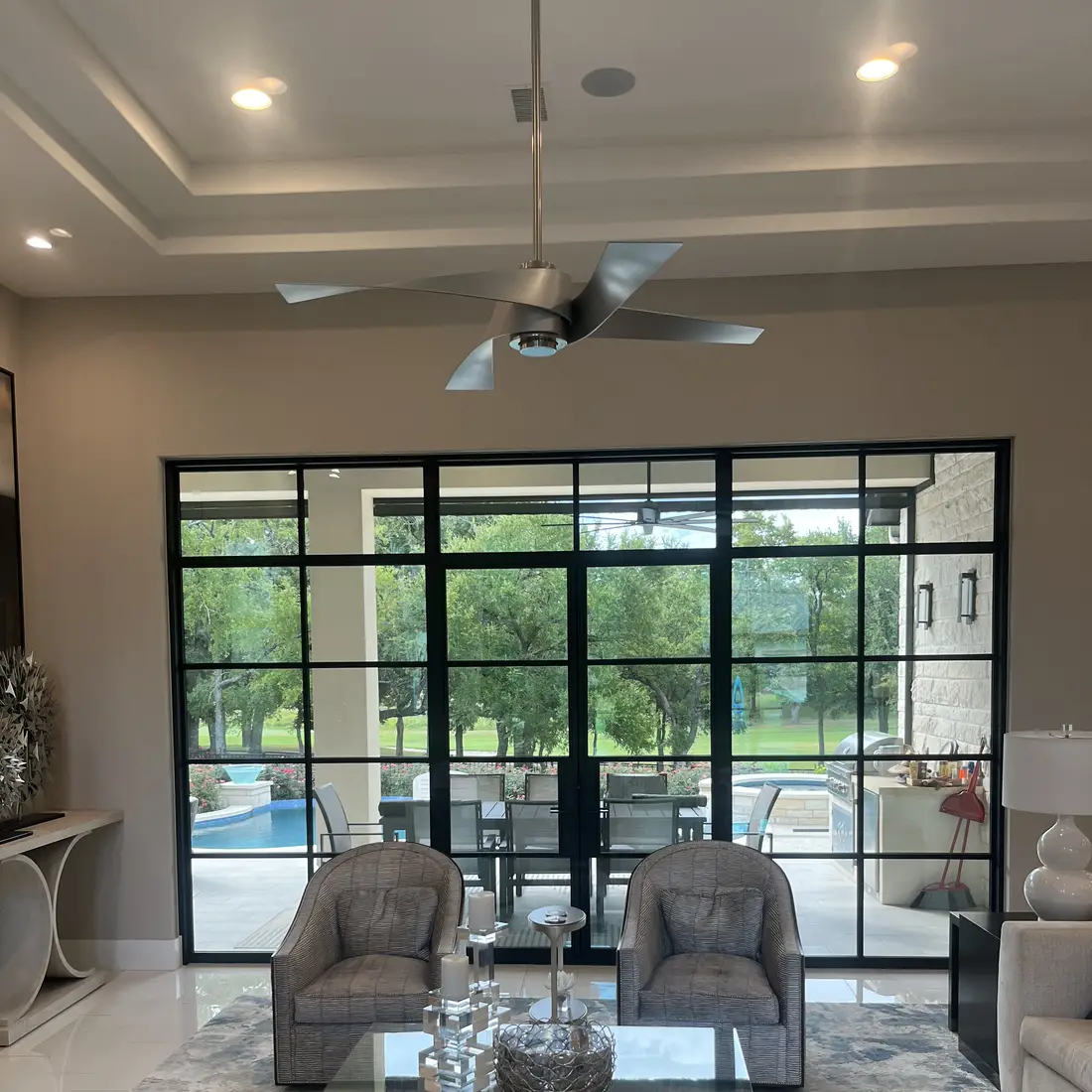 Living room looking through a wall of black framed glass doors to a covered patio, pool and lawn