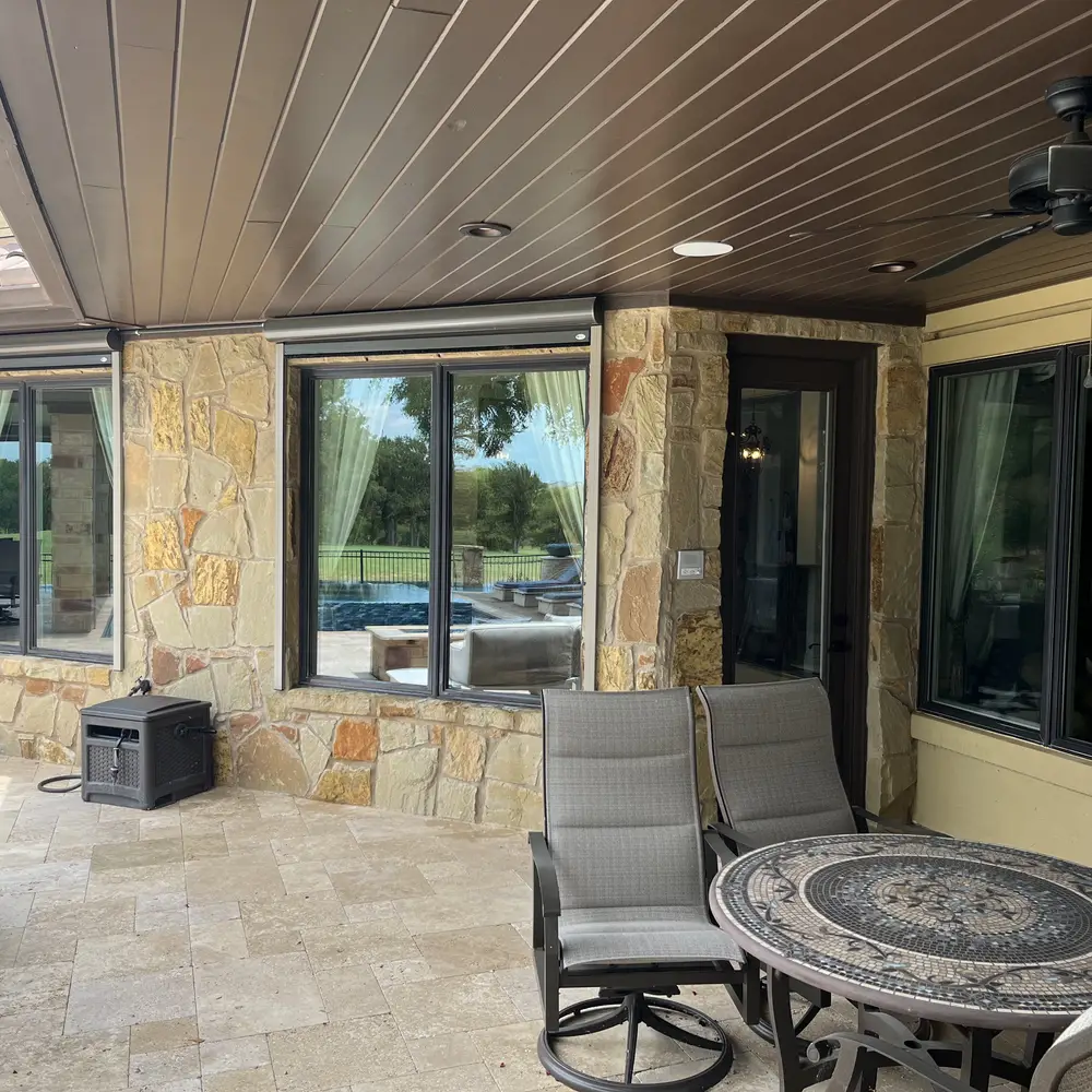 Covered stone patio with sliding glass doors and windows along it, pool visible through the glass