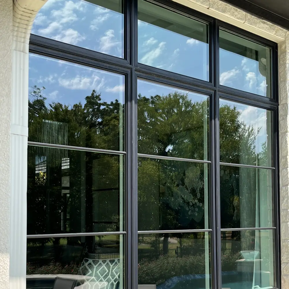 Large multi pane picture window from outside, reflecting sky and trees with the pool area behind
