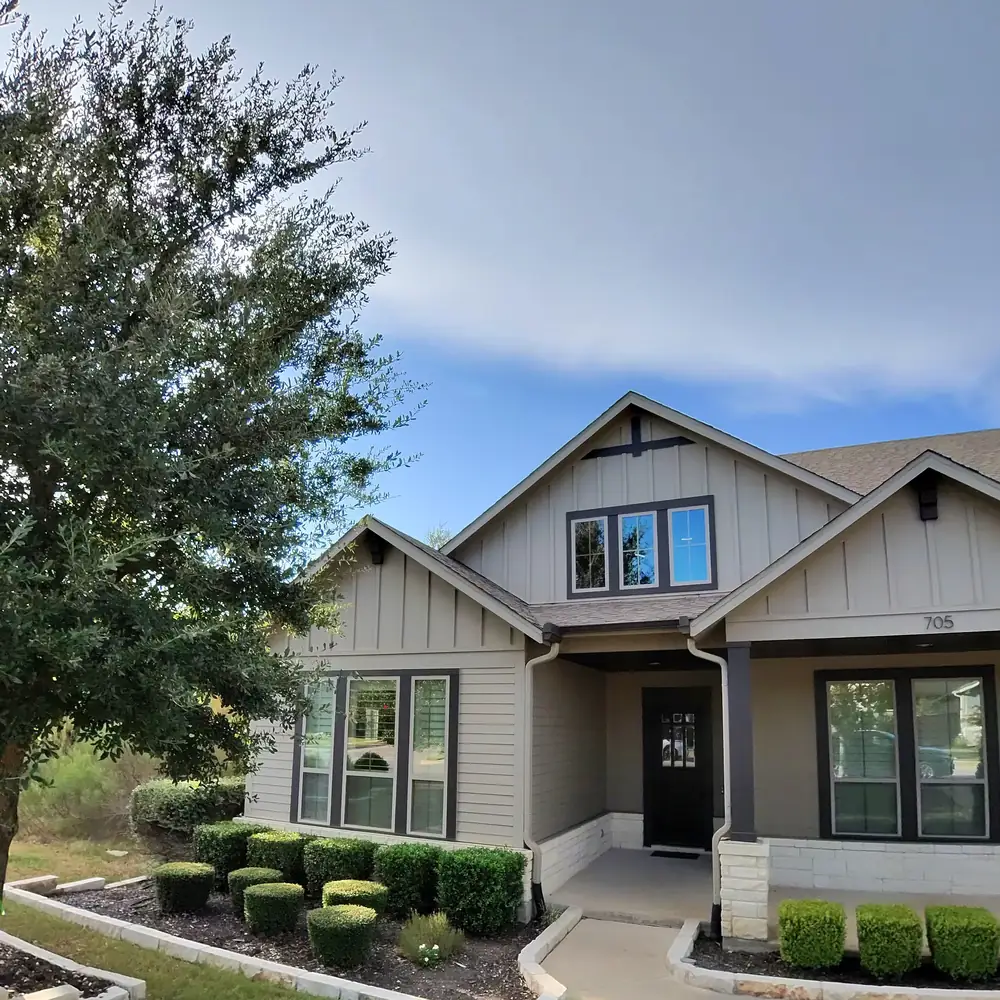 Craftsman style home with board and batten siding and dark framed windows reflecting the front yard trees