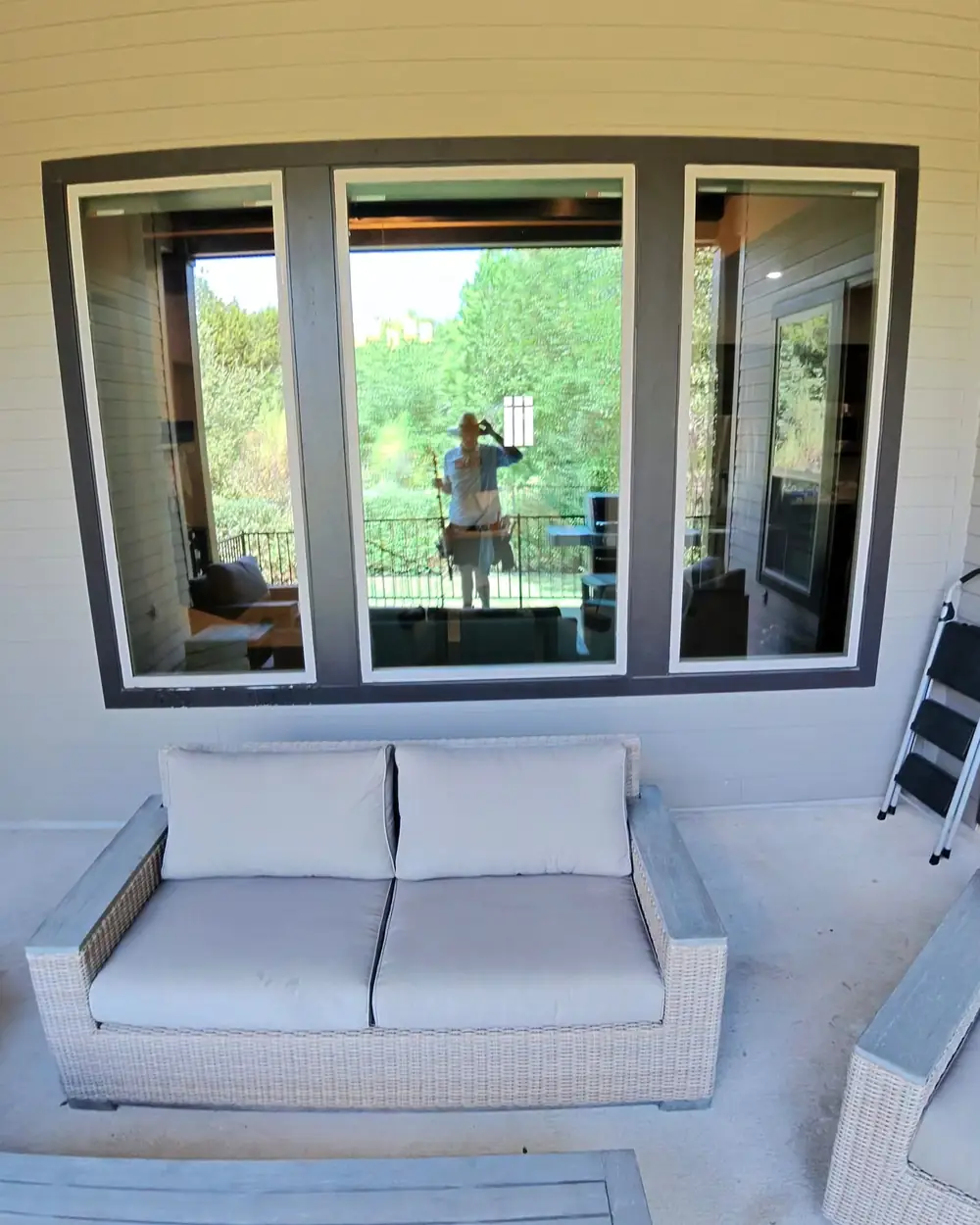 Three panel window on a covered patio with the window cleaner reflected in the clean glass