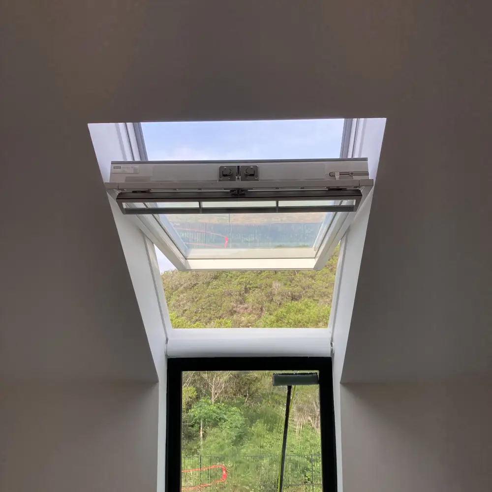 Roof window propped open above a tall window looking out over the treeline