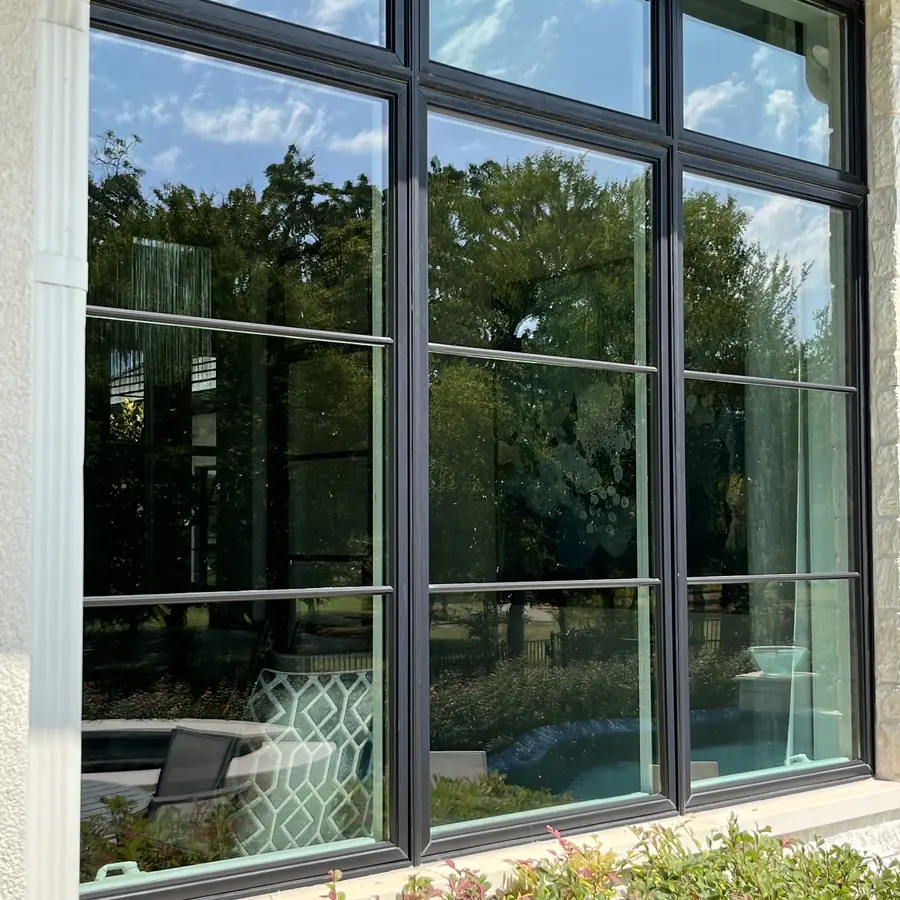 Tall multi pane window wall reflecting trees, with the pool area visible through the glass