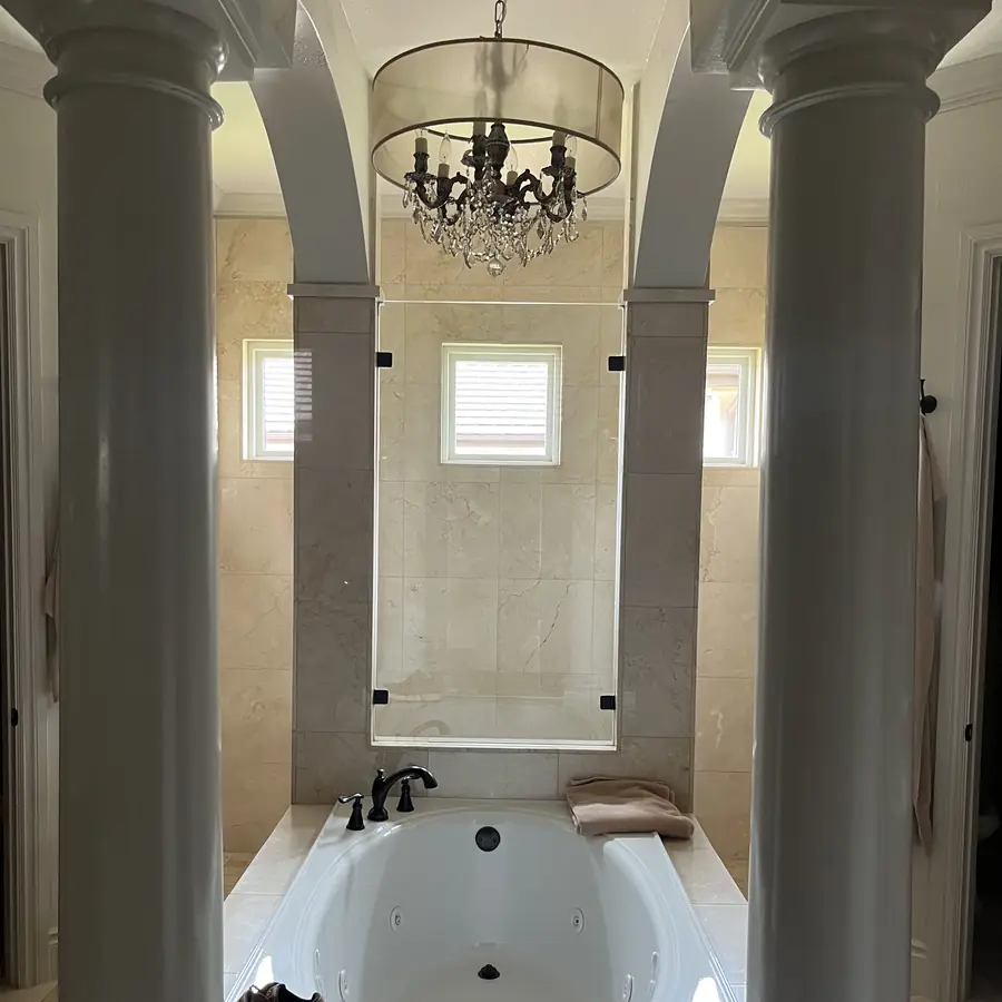 Marble bathroom between stone columns with shuttered windows above the tub