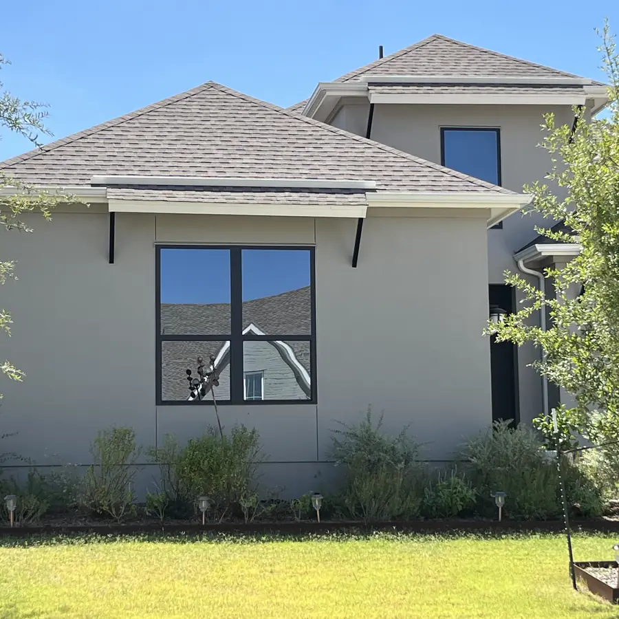 Single story stucco home with dark framed windows and a young live oak on the lawn