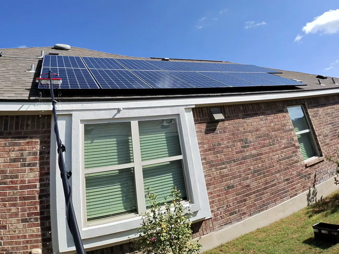 Water-fed pole brush cleaning a roof-mounted solar array on a brick home